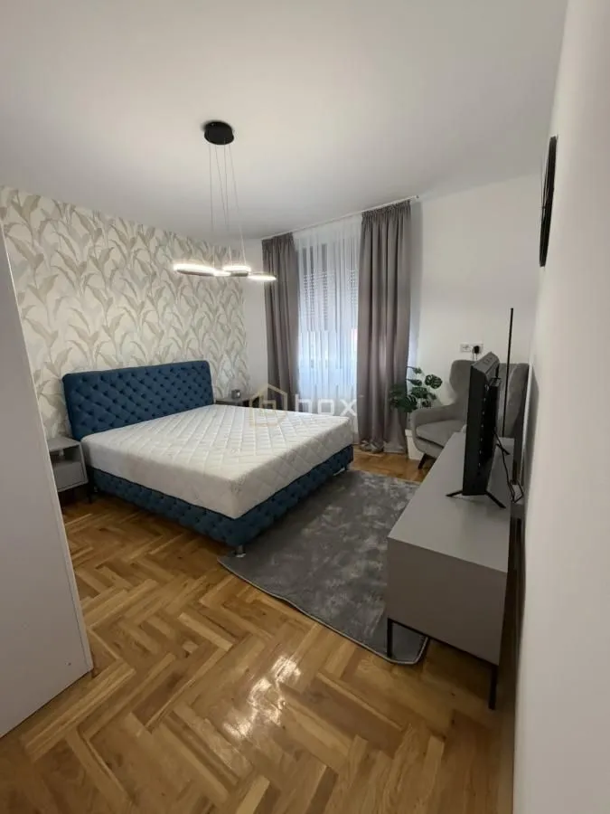 Nameštena spavaća soba sa bračnim krevetom, plakarom i televizorom.