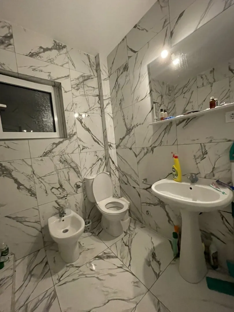 Kupatilo sa pločicama mermernog uzorka, lavaboom i toaletom.
