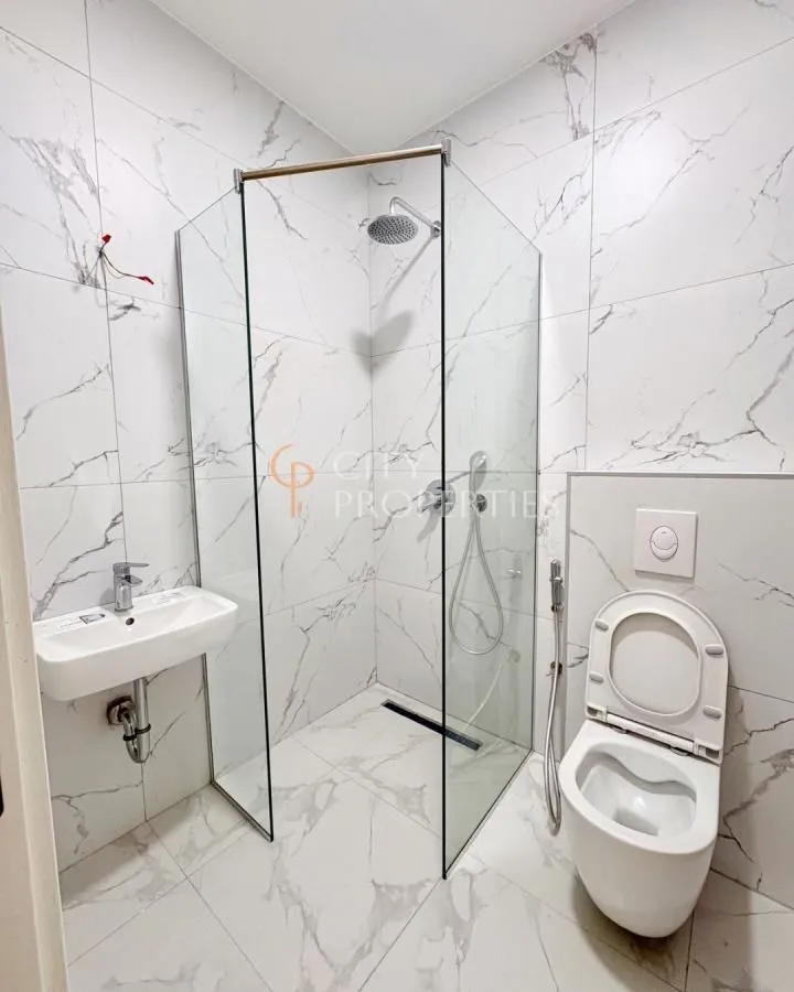 Modern bathroom with a glass-enclosed shower and marble-patterned tiles.