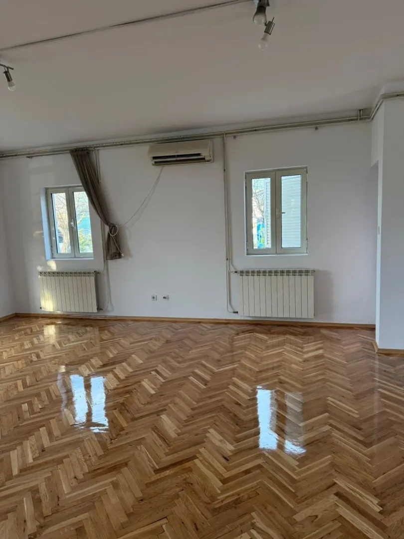 An empty room featuring polished parquet flooring, two windows, and an air conditioner.