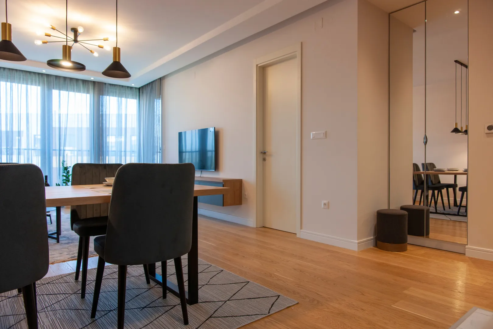 Living room with a dining table, modern lighting, and wooden flooring.