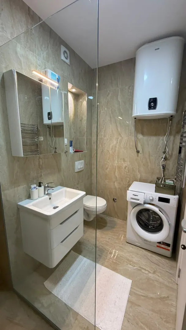 Moderne kupatilo sa umivaonikom, WC šoljom, tuš kabinom i mašinom za veš.