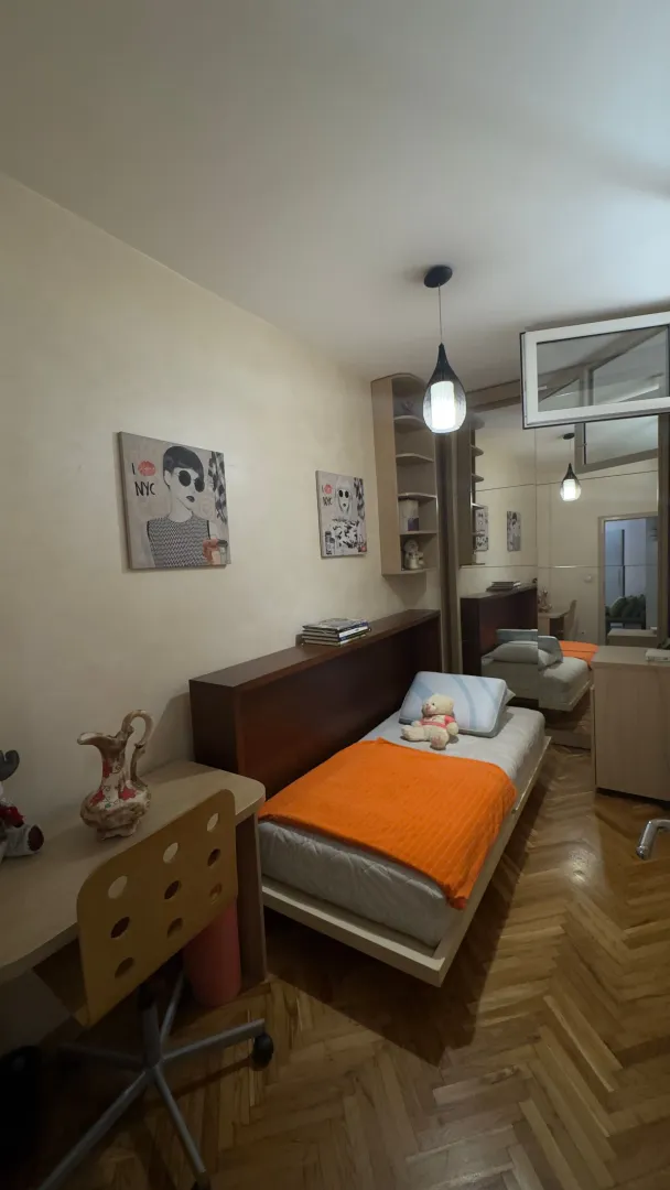 Manja spavaća soba sa krevetom, radnim stolom i velikim ormarom sa ogledalom.