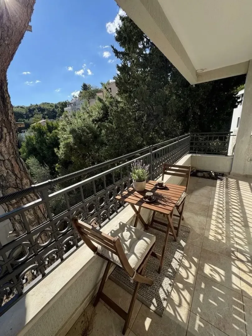 Svijetao i uređen balkon sa stolom, stolicama i pogledom na zelenilo.