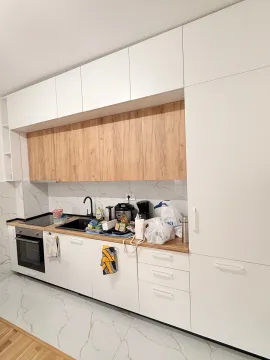 Moderna bijela kuhinja sa drvenim detaljima i neredom na radnoj površini. - image 4