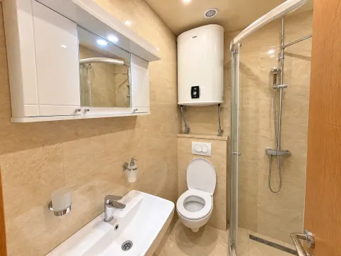 Smaller bathroom tiled in beige with a shower cabin, sink, and toilet. - image 6