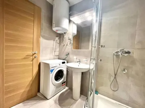 Small bathroom with a sink, shower cabin, water heater, and washing machine. - image 7