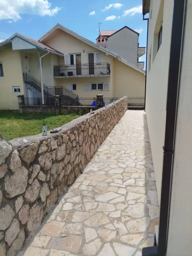Popločana staza sa kamenim zidom u dvorištu kuće.