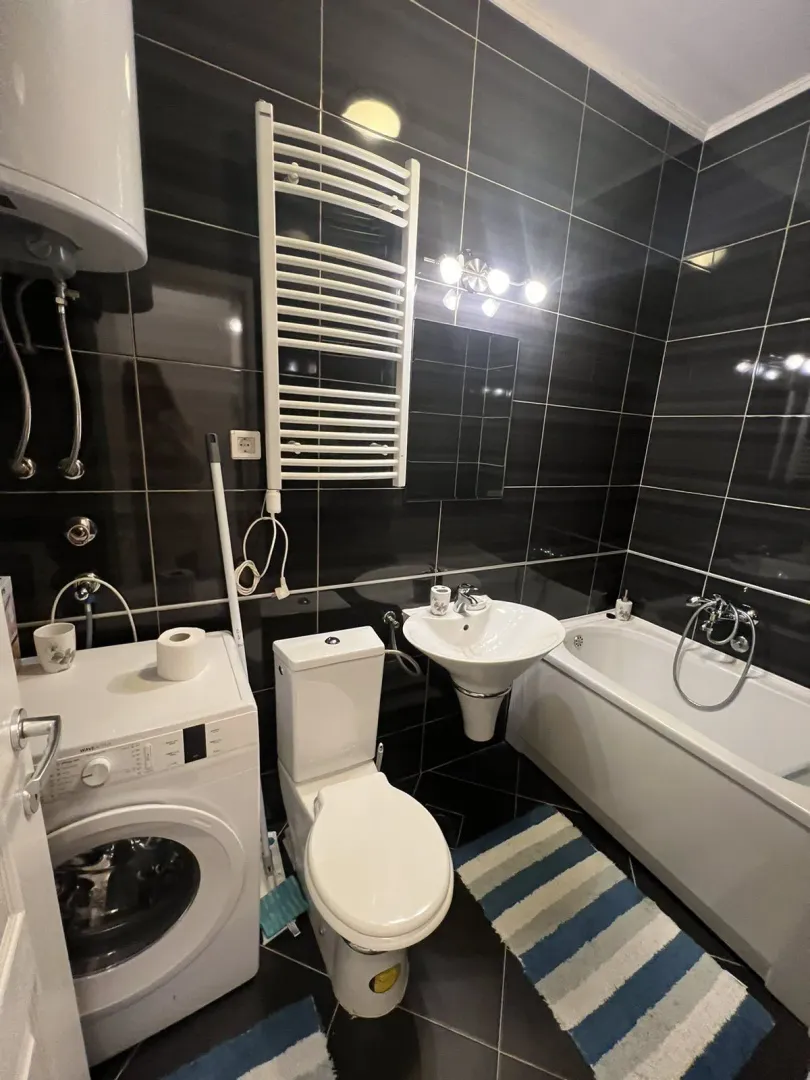A bathroom with black tiles, a bathtub, and a washing machine.