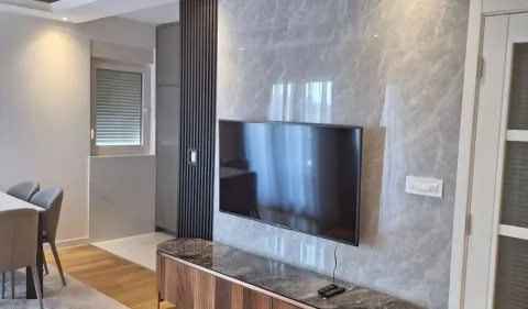 Dnevna soba sa televizorom montiranim na mermerni zid i trpezarijskim stolom u uglu. - image 6