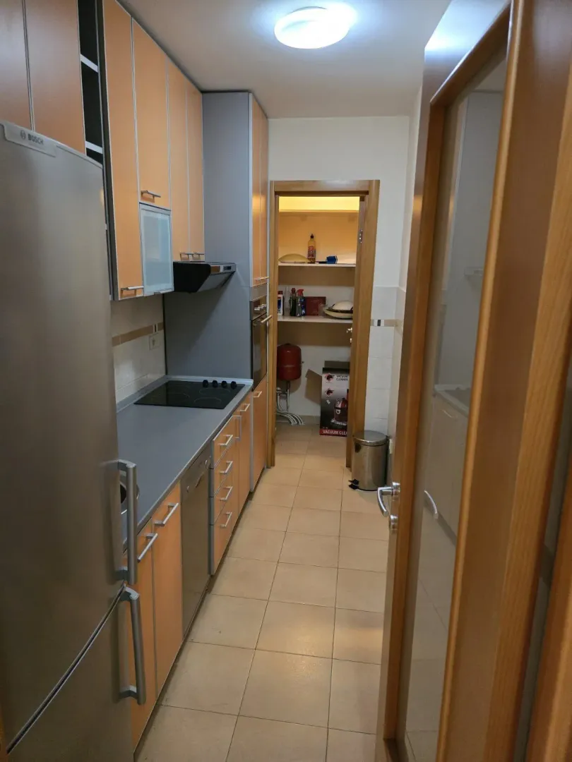 A narrow kitchen featuring light-colored cabinets and a pantry in the background.