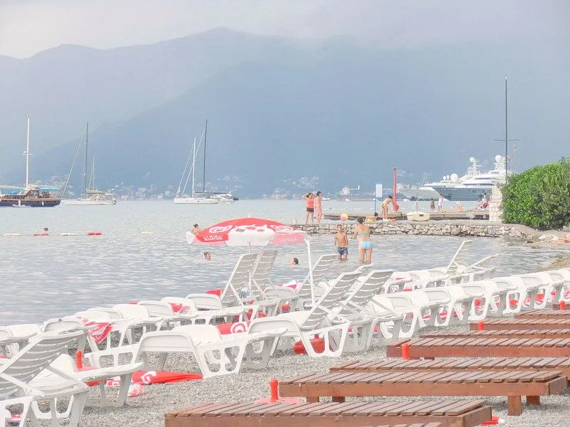 Pogled na plažu sa ležaljkama i more sa brodovima u daljini.