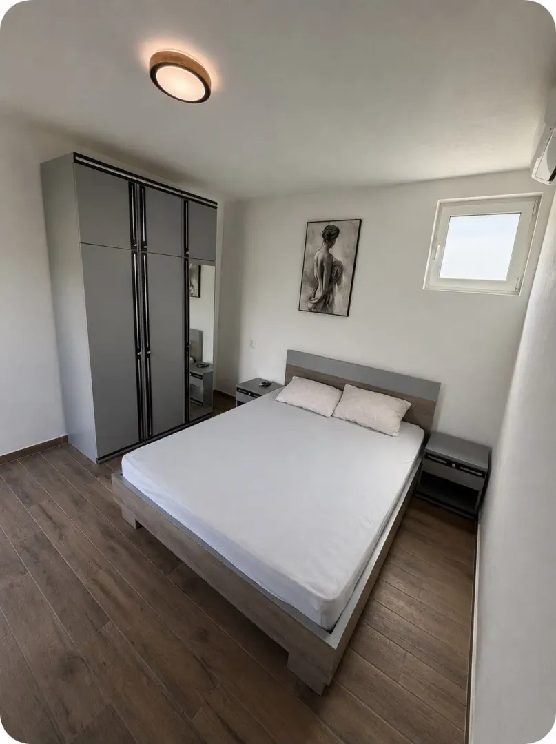 A furnished bedroom with a double bed, wardrobe, and wooden flooring.