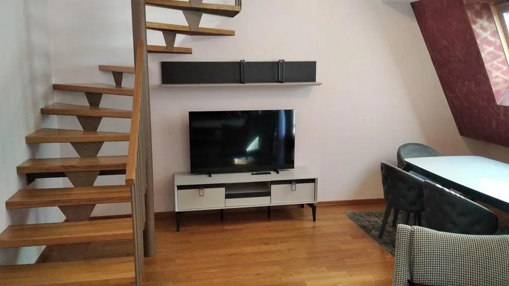 Dnevna soba sa televizorom, trpezarijskim stolom i unutrašnjim stepeništem.