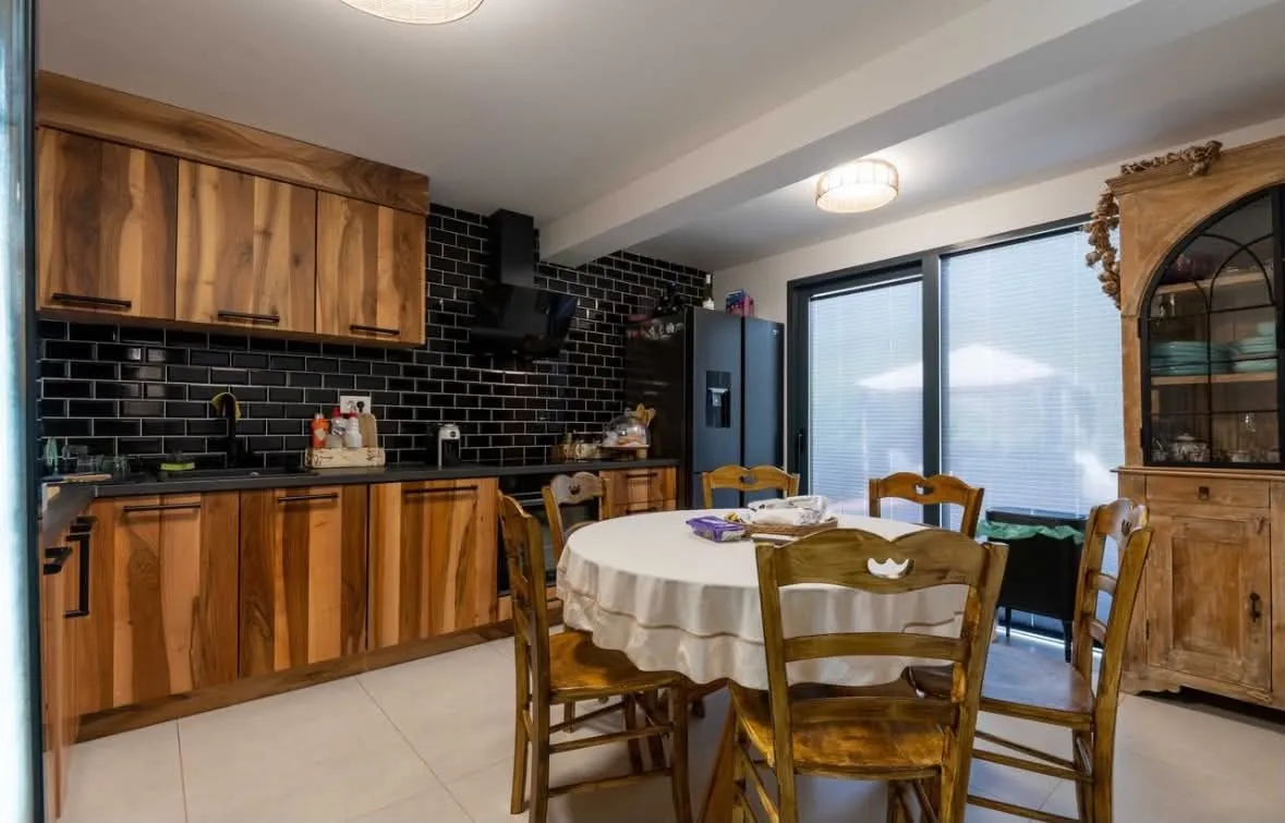 Kitchen with wooden cabinetry, black tiles, and a dining table.