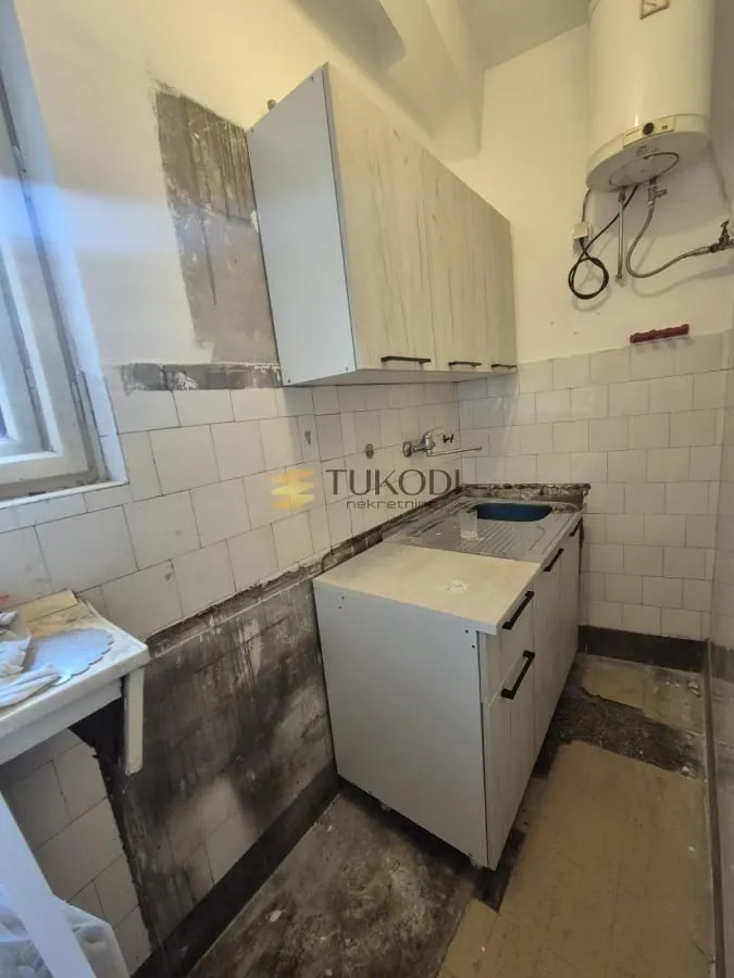 Starija kuhinja sa sudoperom i zidnim ormarićima kojoj je potrebno renoviranje.
