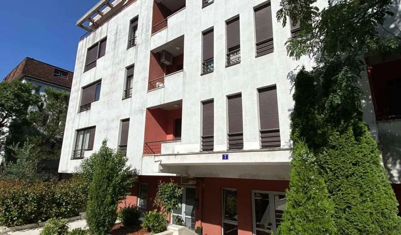 Pogled na fasadu stambene zgrade sa ulazom i zelenilom u okruženju.