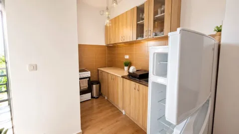 Manja kuhinja sa drvenim elementima i bijelim frižiderom u prednjem planu. - image 6