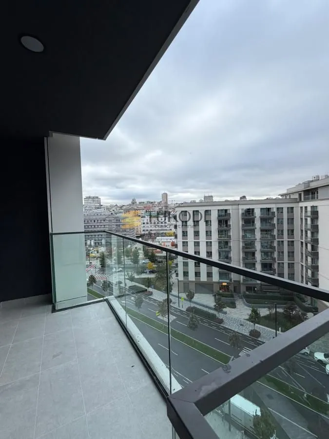 Natkriveni balkon sa staklenom ogradom i pogledom na grad.