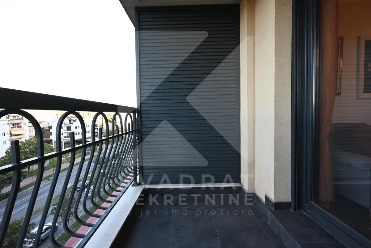 Natkriveni balkon sa metalnom ogradom i pogledom na ulicu.