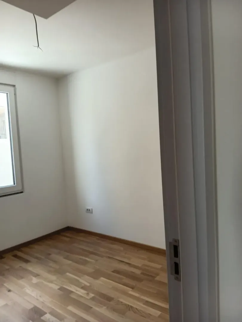 Prazna soba sa parketom i belim zidovima gledana kroz otvorena vrata.