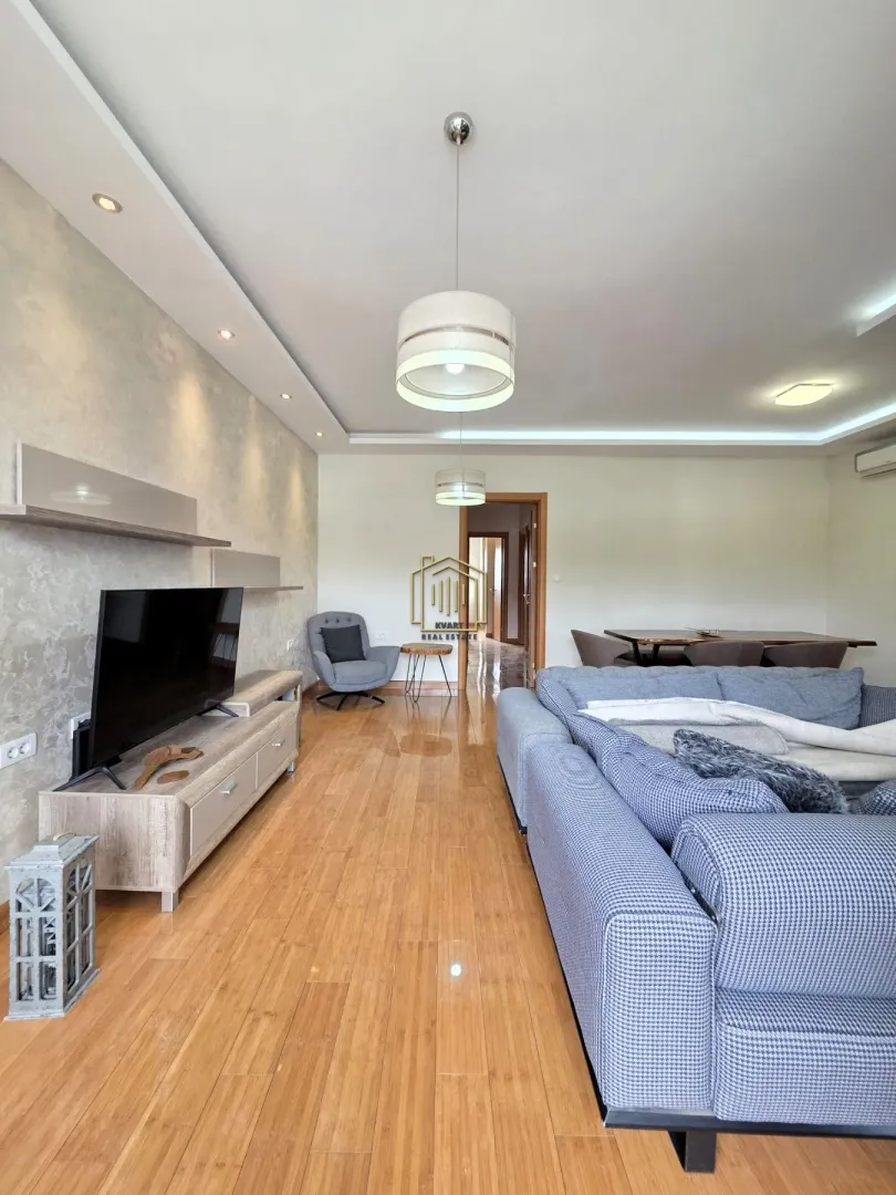 Spacious living room with a sofa set, television, and dining area in the background.
