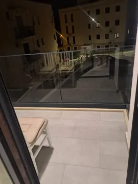 Small tiled balcony with a glass railing and a chair in the evening. - image 8