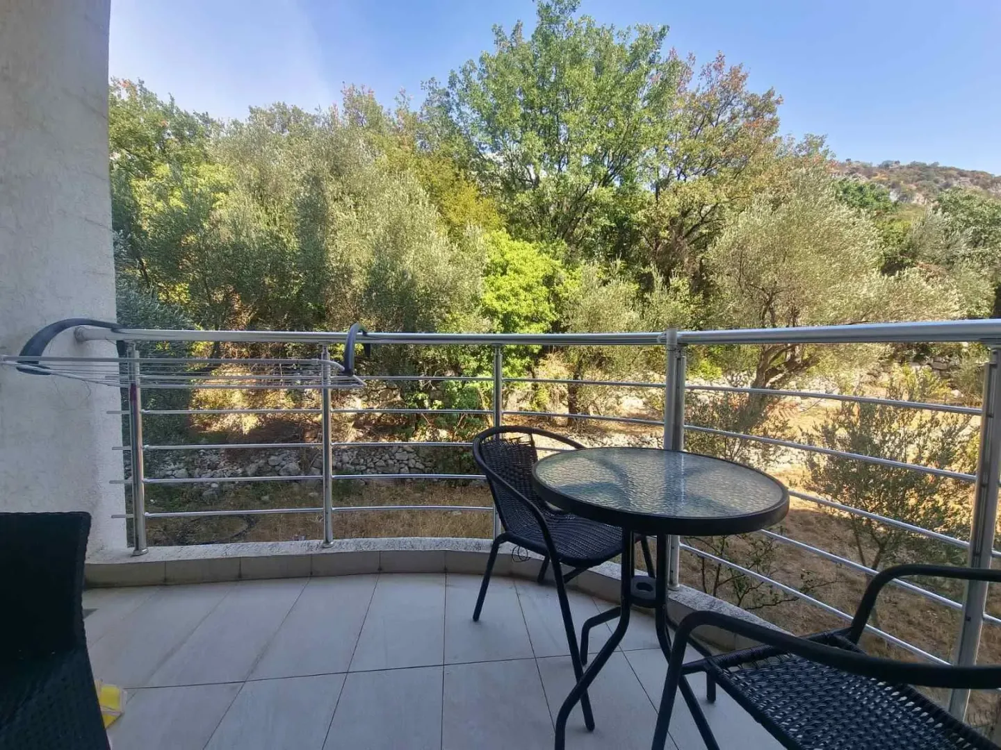 Small furnished balcony with a table, chairs, and a view of greenery.