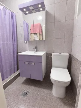 Kupatilo opremljeno umivaonikom sa ormarićem, toaletom i tuš kabinom sa ljubičastom zavesom. - image 4