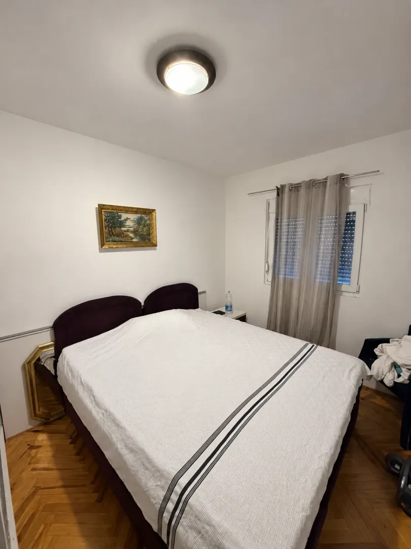 Bedroom with a double bed, parquet flooring, and a window with curtains.
