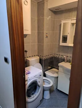 Manje kupatilo sa sanitarijama, veš mašinom i bijelim ormarićem sa ogledalom. - image 5