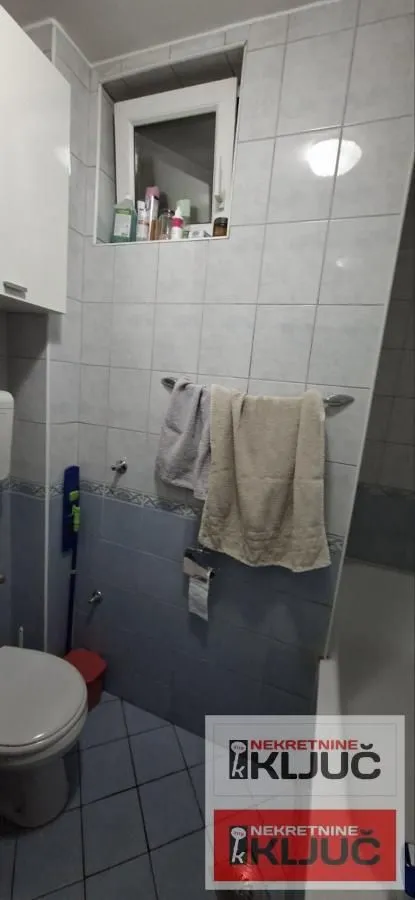 Pogled na dio kupatila sa WC šoljom, pločicama i prozorom.