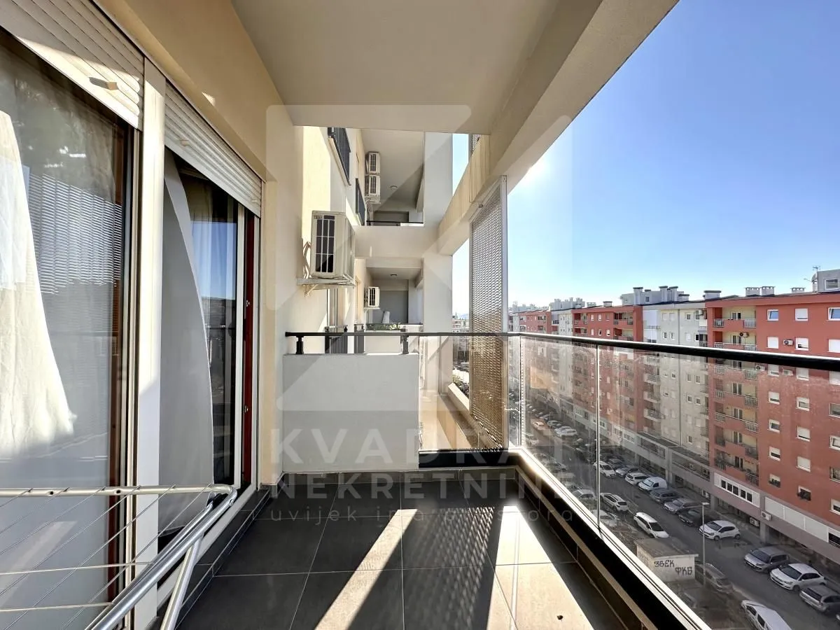 Natkriveni balkon sa staklenom ogradom i pogledom na ulicu i zgrade.