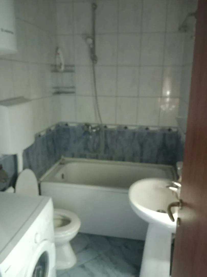Jednostavno kupatilo sa kadom, lavaboom, toaletom i veš mašinom.
