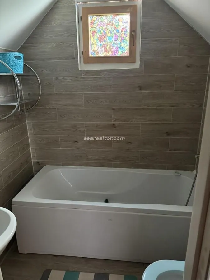 Kupatilo sa kadom i zidnim pločicama u imitaciji drveta pod kosim krovom.