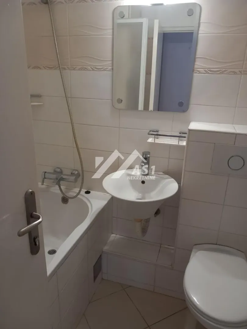 Smaller bathroom equipped with a bathtub, washbasin, mirror, and toilet bowl.