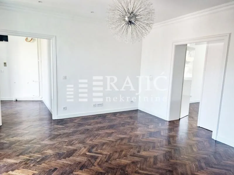 Empty bright room with dark parquet flooring and a decorative chandelier.