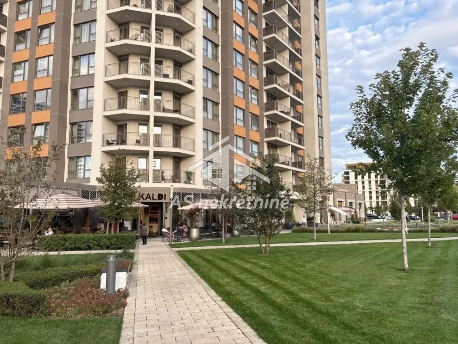 Pogled na spoljašnjost stambene zgrade sa uređenim dvorištem i stazom.