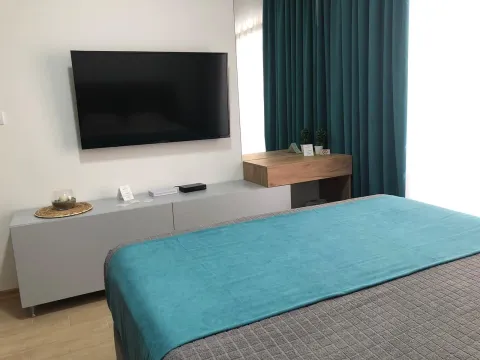 Namještena spavaća soba sa bračnim krevetom, TV-om i plavim zavjesama. - image 4