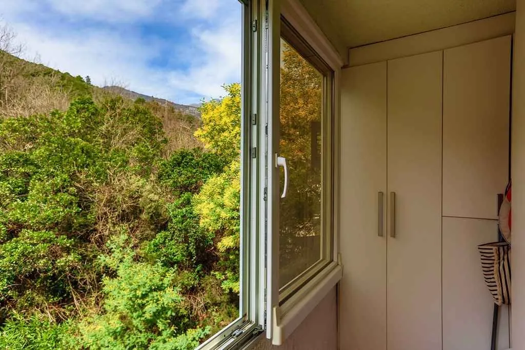 Open window on a glazed balcony looking out onto lush greenery.