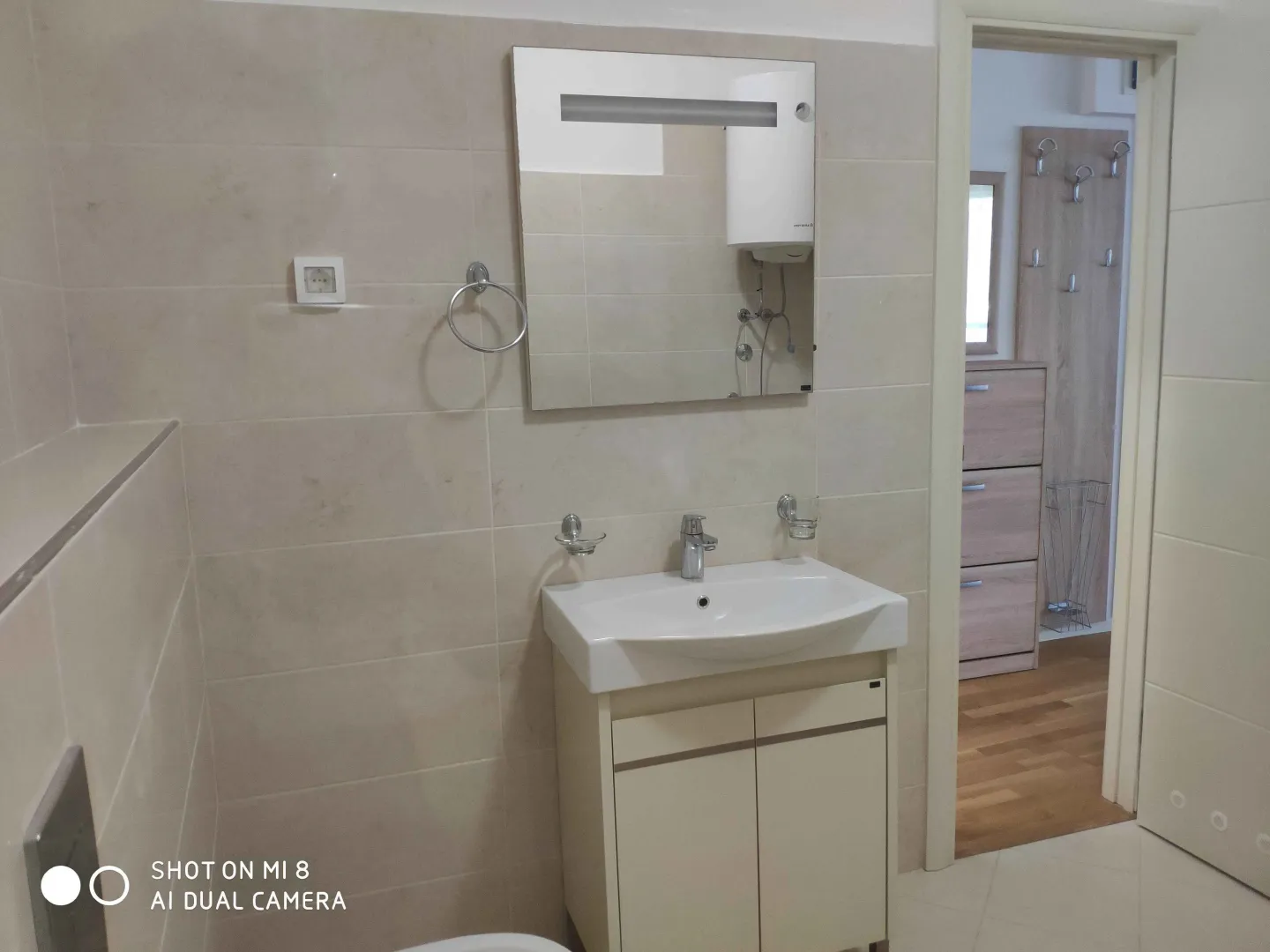 Bright bathroom with a sink, mirror, and a view of the hallway.