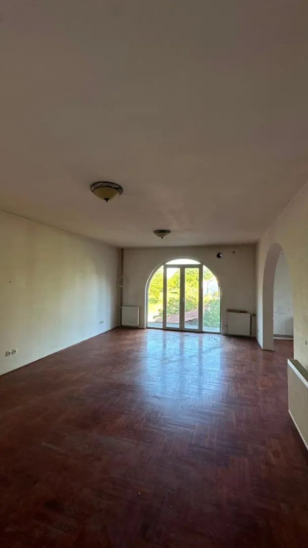 Empty room with wooden parquet flooring and arched balcony doors.