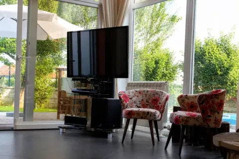 Living room with a large TV, two floral patterned armchairs, and a view of the yard. - image 8