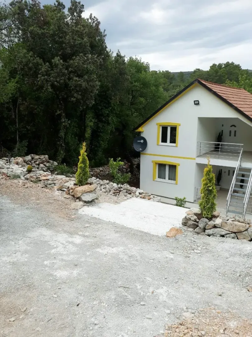 Dvospratna kuća sa bijelom fasadom i kamenim detaljima u dvorištu.