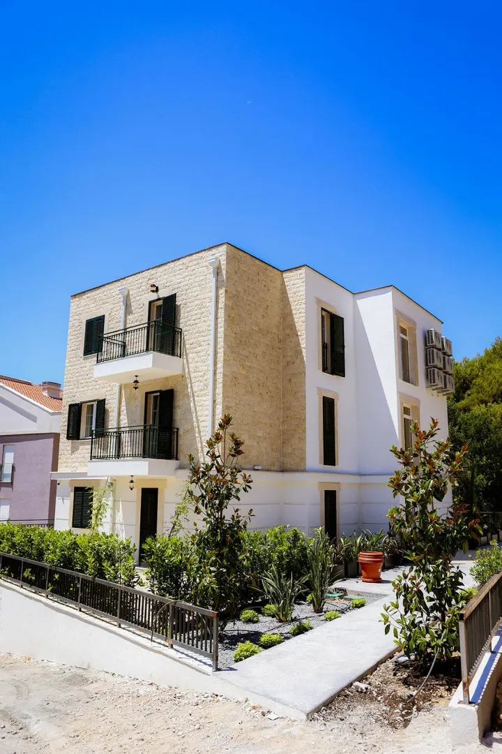Spoljašnji izgled moderne stambene zgrade sa uređenim dvorištem i balkonima.