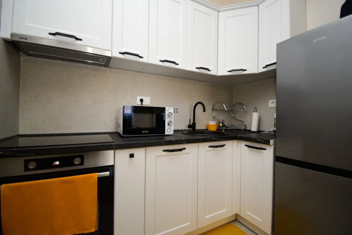 Compact kitchen with white cabinets, built-in oven, and a refrigerator.