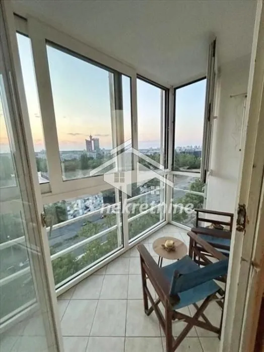 Enclosed balcony with seating furniture and a city view.