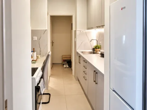 View of a narrow kitchen with white cabinets and a refrigerator. - image 7