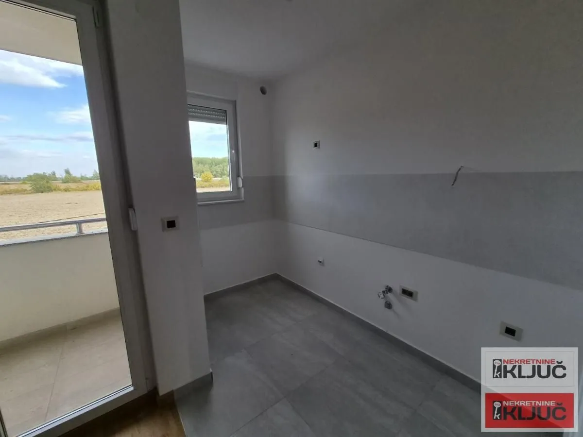 Prazna prostorija sa izlazom na balkon i priključcima za kuhinju.