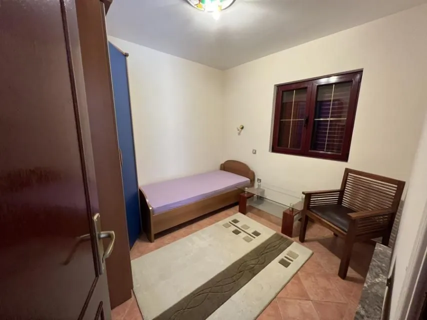 A simply furnished bedroom with a single bed, a wardrobe, and a wooden armchair.